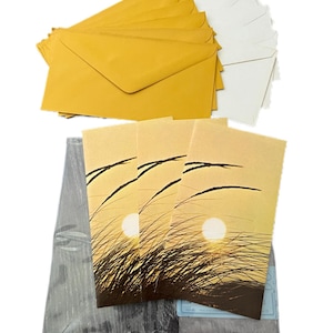 May include: A collection of stationery items, including yellow and white envelopes, and cards with a sunset design. The cards are packaged in a clear plastic wrap. The letters "AGC" are visible on the packaging.