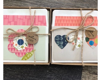 Op de afbeelding: Twee Hallmark 8 Notes dozen gebonden met touw. De ene set heeft een groot roze bloemmotief, de andere drie hartmotieven. De dozen zijn lichtbruin en de kaarten hebben kleurrijke patronen.