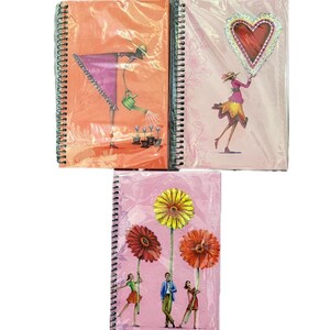 May include: Three spiral-bound notebooks featuring illustrated covers. The top left notebook is orange with a figure watering plants. The top right is light pink with a figure holding a heart. The bottom notebook is pink with three large flowers.