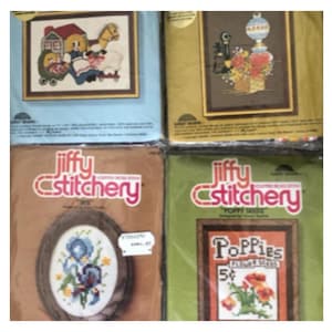 May include: Four vintage Jiffy Stitchery counted cross-stitch kits. The kits feature framed designs of a house with figures, a lamp with flowers, iris flowers, and poppies. The kits are in their original packaging.