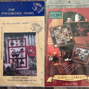 May include: Two sewing pattern books. The left book is titled "The Patchwork Angel" and features a quilt, a t-shirt, and a pillow with applique designs. The right book is titled "Barnyard & Cow Country" and features cow-themed quilt patterns.