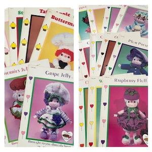 May include: A collection of vintage crochet pattern booklets featuring whimsical doll designs. The covers showcase colorful illustrations of the dolls, each with a unique outfit and name, such as "Grape Jelly" and "Raspberry Fluff". The booklets are stacked, displaying their titles.