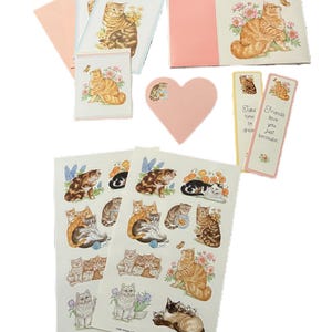 May include: A collection of cat-themed stationery and stickers. Includes greeting cards, a heart-shaped tag, bookmarks, and sticker sheets. The designs feature illustrations of cats with flowers and butterflies, in shades of orange, brown, and white.