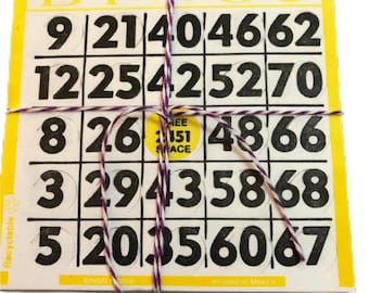 Può includere: Un mucchio di cartelle della tombola con bordo giallo e numeri neri. Le carte sono legate insieme con uno spago viola e bianco. La parola "BINGO" è visibile sulle carte.