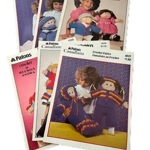 May include: A stack of vintage Patons crochet pattern booklets. The covers feature images of children with crochet dolls and outfits. The booklets are titled "All Dressed Up", "Crochet Cuties", and "Beehive Astra".