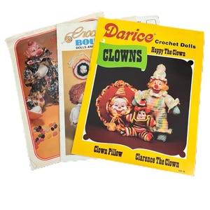 May include: Three vintage crochet pattern books featuring clown designs. The books have colorful covers with images of crocheted clown dolls and pillows. Titles include "Darice CLOWNS" and "Crochet Dolls".