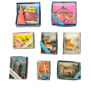 May include: A collection of vintage miniature dioramas in small boxes. Each box features a different scene, including a woman in a dress, circus performers, deer, a couple, a ballerina, and a horse. Some boxes have "Happy Birthday" ribbons.