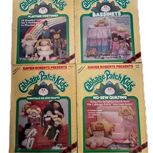 May include: Four boxes of Cabbage Patch Kids sewing patterns. The boxes are yellow with red and green plaid trim. The boxes feature different themes: Playtime Costumes, Bassinets, Christmas No-Sew Crafts, and No-Sew Quilting.