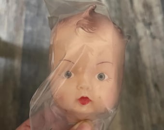 Vintage doll head. New old stock.  Life like eyes brown painted hair curl on top. Head approximately 4”