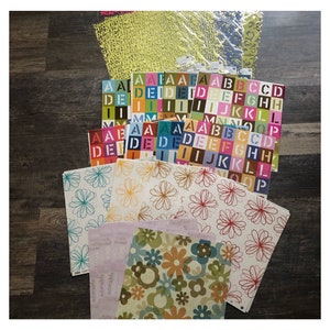 May include: A collection of colorful patterned scrapbook paper featuring floral designs, alphabet letters, and a yellow patterned sheet.
