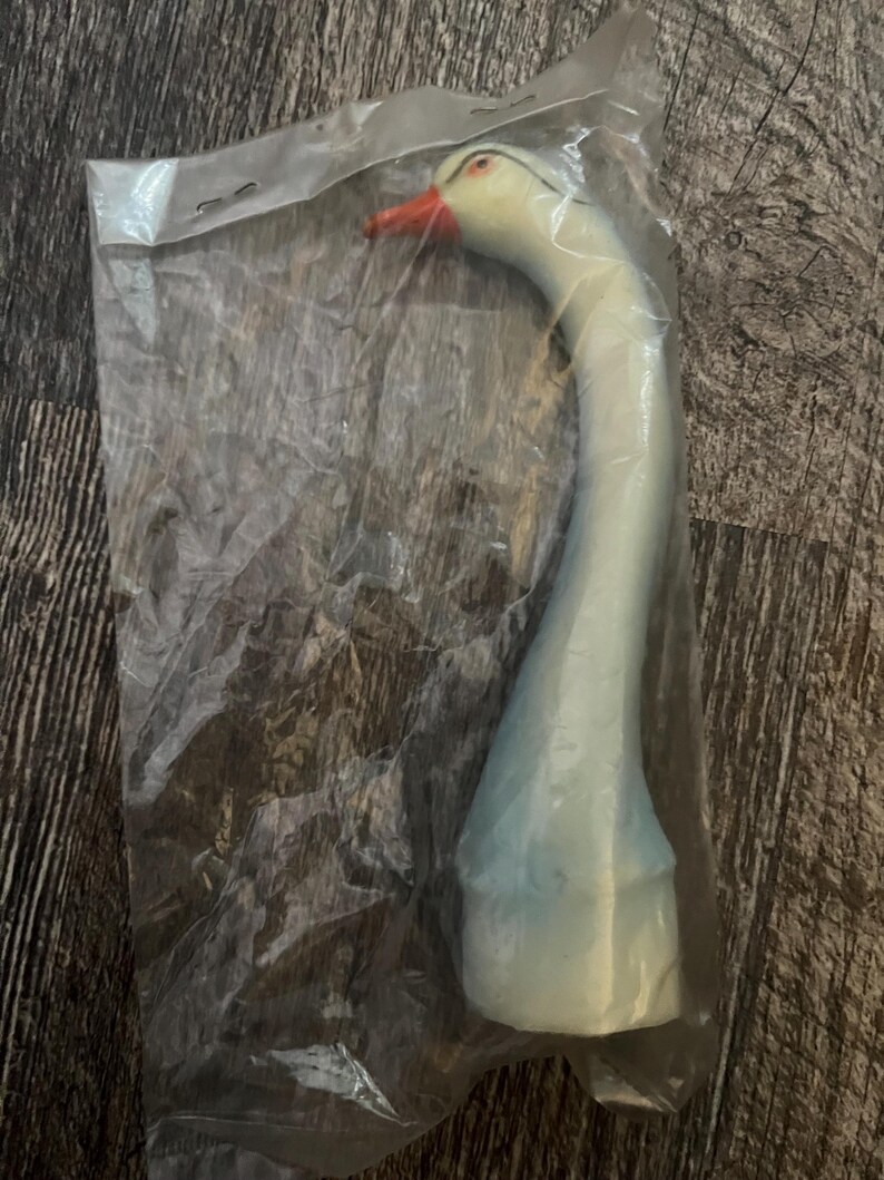 May include: A white plastic goose decoy with a red beak and black eyes. The decoy is in a clear plastic bag.