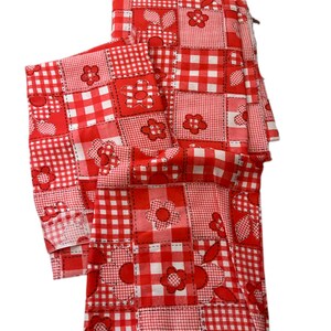 May include: Red and white patchwork fabric with a gingham pattern and floral appliqués. The fabric is folded and appears to be a set of kitchen linens, such as a tablecloth and napkins. The design is a mix of squares and floral shapes.