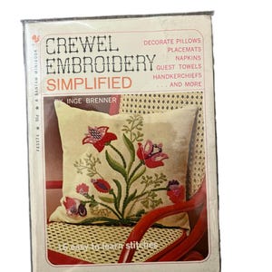 May include: A vintage book titled "Crewel Embroidery Simplified" by Inge Brenner. The cover shows a cream cushion with red and pink floral embroidery. The book promises 17 easy-to-learn stitches for decorating cushions, placemats, napkins, and more.