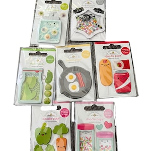 May include: Assortment of Doodle-Pops and Shaker-Pops cardstock stickers in various designs. The stickers include a jar of cookies, a spider, pickles, a frying pan with eggs and bacon, a corn dog and soda, vegetables, and jars of sprinkles.
