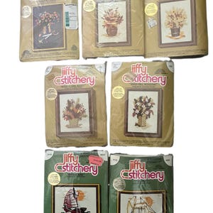 May include: A selection of Jiffy Stitchery cross-stitch kits, featuring framed floral and sailing ship designs. The packaging is tan and green, with the Jiffy Stitchery logo in red and white. The kits are for embroidery.