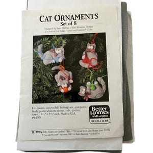 May include: A craft kit for making cat ornaments. The kit includes felt, yarn, pom poms, beads, whiskers, ribbon, bells, and patterns. The ornaments are approximately 4.5 inches by 3.5 inches. The kit is designed by Janet Harlow for Better Homes and Gardens Book Clubs.