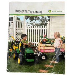 May include: A catalog cover with the text "2010 ERTL Toy Catalog" and the John Deere logo. The image shows children playing with toy tractors and a wagon on a grassy lawn. The toys are green and yellow.