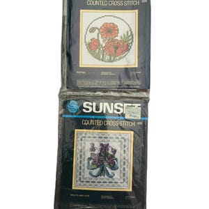 May include: Two Sunset counted cross stitch kits. One depicts red poppies, the other violets and lace. The kits are in their original packaging, with the Sunset logo and product numbers visible.