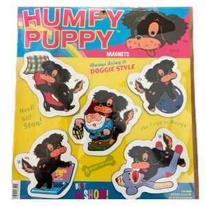 May include: A sheet of Humfy Puppy magnets featuring black and tan cartoon dogs in various poses. The magnets include phrases like "Always doing it Doggie Style" and "The Urge to Merge." The sheet is yellow, blue, and pink.