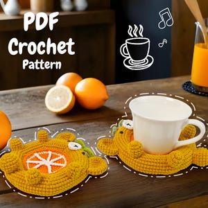 May include: Two crocheted orange and yellow bear-shaped coasters with a cup of coffee on one of them. The coasters are on a wooden table with oranges and lemons in the background. The text "PDF Crochet Pattern" is at the top of the image.