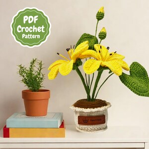 May include: A crocheted yellow flower arrangement in a white pot with a brown label that says "Hand Made". The arrangement is on a white shelf with a stack of books.