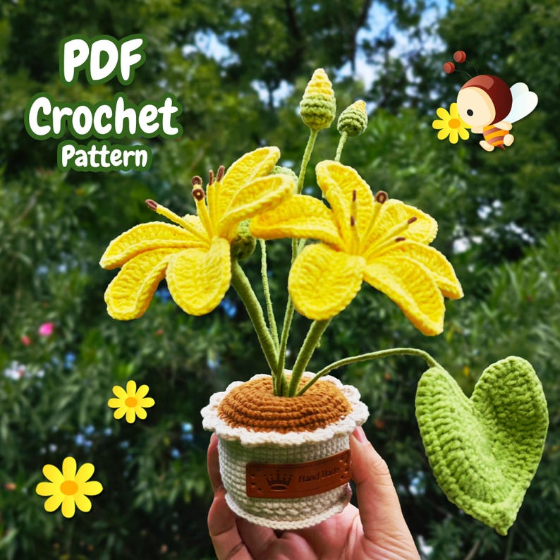 May include: A crocheted yellow flower arrangement in a brown and white pot with a green leaf. The pot has a brown label with the text "Hand Made" and a crown symbol. The flowers are in a hand holding the pot.