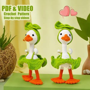 May include: Two crocheted green and white goose amigurumi toys with green bows. The toys are standing on a green surface with a heart shape above them. The text "PDF & VIDEO Crochet Pattern Step-by-step videos" is at the top of the image.