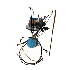May include: A blue glass pendant necklace with a black cord and a silver charm. The pendant is round and has a white design on it. The necklace is displayed on a white card with a picture of a building and a statue.