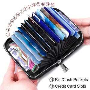 May include: Black leather zippered wallet with 12 credit card slots and 2 bill pockets. The wallet is open and the credit card slots are visible.