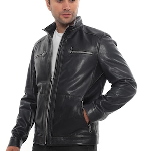 Puede incluir: Chaqueta de cuero negra con cuello alzado, cierre de cremallera y múltiples bolsillos con cremallera. La chaqueta tiene un diseño clásico y un acabado texturizado. El modelo lleva una camiseta blanca.