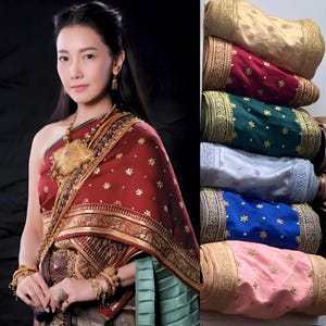 May include: A woman in traditional Thai attire, featuring a red and gold patterned shawl. Stacked, colorful silk bolsters with gold embroidery and floral accents are displayed in shades of gold, red, green, light blue, blue, and pink.