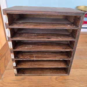 May include: A dark brown wooden organizer with six horizontal shelves. Each shelf is labeled on the left side with the days of the week, starting with Monday at the top and ending with Saturday at the bottom, printed in black text on white labels.