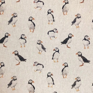 May include: A beige fabric with a repeating pattern of black and white puffins. The puffins are depicted in a realistic style with their beaks open.