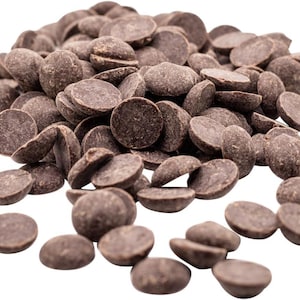 May include: A collection of dark brown chocolate chips, each in a flat, disc shape. The chips are scattered, with some overlapping, creating a textured surface. The image is well-lit, highlighting the details of the chocolate.