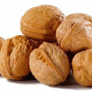 May include: A collection of brown walnuts with rough, textured shells. The nuts are piled together, with some partially visible. The lighting is good, showing the details of the nut's surface.
