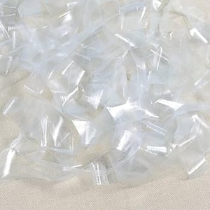 Może przedstawiać: Zbliżenie na stos małych, przezroczystych plastikowych toreb. Torby są w większości prostokątne z zamkniętą górą i są lekko przezroczyste, tworząc efekt połysku. Torby są rozrzucone i zachodzą na siebie.