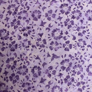 May include: Purple floral fabric with a white background. The fabric has a batik design with a repeating pattern of small flowers.