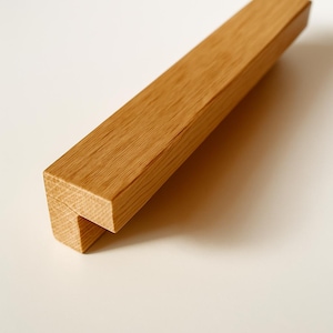 Könnte beinhalten: Ein rechteckiger Holzschrankgriff mit natürlicher Oberfläche. Der Griff hat eine hellbraune Farbe und ein schlichtes, modernes Design. Der Schrankgriff ist etwa 15 cm lang.