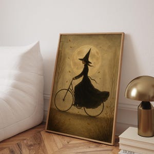 May include: A framed art print depicts a witch riding a bicycle. The witch is wearing a black dress and hat, silhouetted against a full moon. The artwork has a vintage, whimsical style, with autumn leaves and trees.