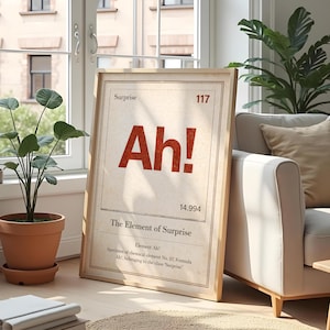 Könnte beinhalten: Ein gerahmter Druck mit dem Text "Ah!" in fetten roten Buchstaben. Der Druck trägt die Aufschrift "The Element of Surprise" und enthält wissenschaftliche Details. Der Rahmen ist helles Holz, und der Druck lehnt an einem weißen Sofa.