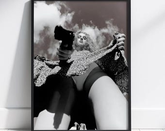 Può includere: Stampa incorniciata in bianco e nero raffigurante una persona che tiene in mano una pistola, vista dal basso. La persona indossa un vestito a fantasia floreale. Lo sfondo mostra un cielo nuvoloso.