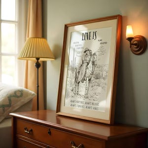 K&ouml;nnte beinhalten: Ein gerahmter Druck mit einer Schwarzwei&szlig;illustration eines Paares, das auf Pferden durch eine W&uuml;stenlandschaft reitet. Der Text "Love is Pure Devoted" befindet sich oben auf dem Druck. Der Text "Always Nurturers, Always Believes, Always Forgives, Always Heals" befindet sich unten auf dem Druck.