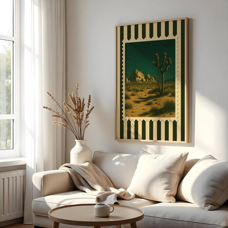 May include: A framed art print featuring a desert landscape with a Joshua tree under a starry night sky. The artwork is designed to resemble a postage stamp, with a green and cream striped border. The print is displayed in a living room setting.