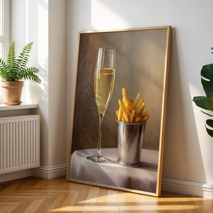 May include: A framed painting depicts a champagne flute filled with bubbly liquid and a metal cup overflowing with golden french fries. The artwork is leaning against a white wall, with a fern in a pot visible in the background.