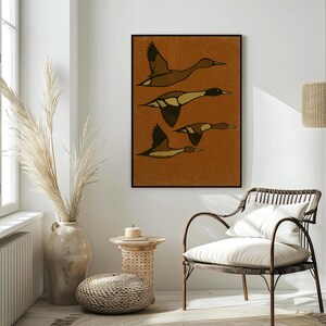 Pu&ograve; includere: Una stampa artistica incorniciata con quattro anatre stilizzate in volo. Gli uccelli sono raffigurati in tonalit&agrave; di marrone e nero su uno sfondo strutturato color ruggine. L'opera d'arte &egrave; esposta in una stanza con una palette di colori neutri, tra cui una sedia intrecciata e un vaso decorativo.
