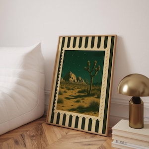 May include: Framed art print featuring a desert landscape with a Joshua tree under a starry night sky. The artwork is framed with a green and cream border, creating a vintage aesthetic. The print is leaning against a white wall.