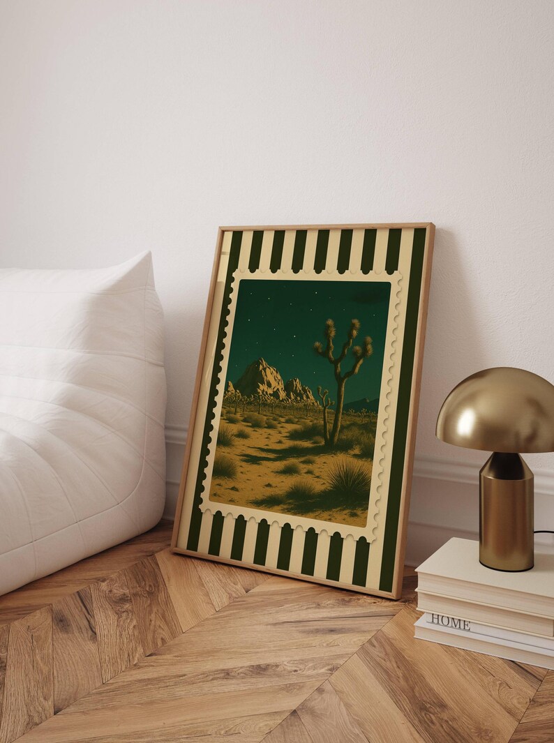 May include: Framed art print featuring a desert landscape with a Joshua tree under a starry night sky. The artwork is framed with a green and cream border, creating a vintage aesthetic. The print is leaning against a white wall.