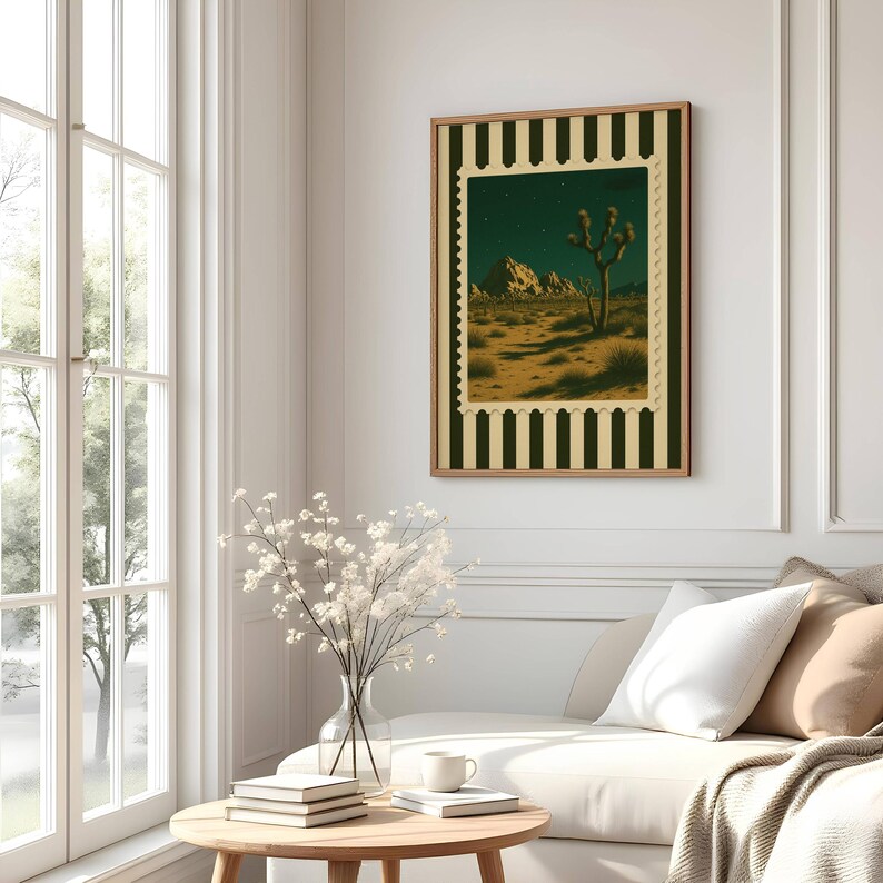 May include: A framed art print featuring a desert landscape with a Joshua tree under a starry night sky. The artwork is framed with a brown border and a decorative stamp-like edge. The print is displayed on a white wall above a white couch.