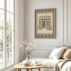 May include: A framed black and white print of a cafe scene. The artwork features a cafe exterior with tables and chairs, and the word "CAFE" above the entrance. The print is surrounded by a black and white striped border.