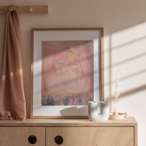 May include: A framed painting of a stage with pink and white curtains and a crowd of people in the background. The painting is hanging on a light wood wall with a brown scarf hanging on hooks above it. A white ceramic vase and a white candle are on the shelf below the painting.